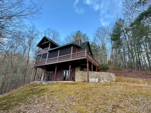 rear view of house featuring a deck, a chimney, a yard, and a sunroom