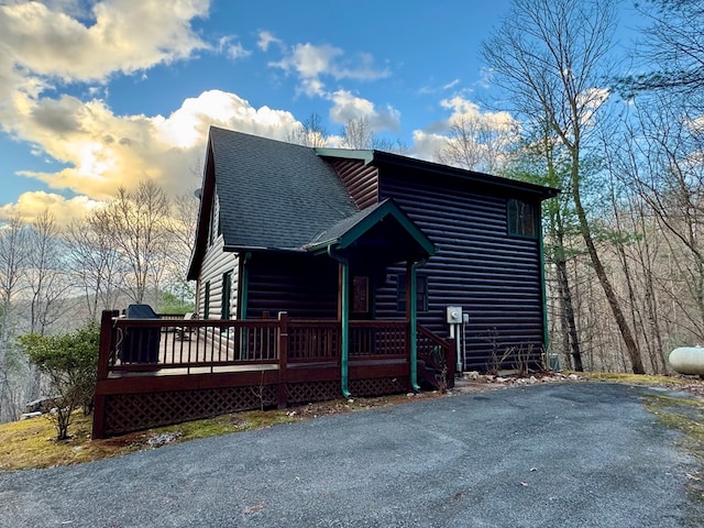 view of front of house with faux log siding, a shingled roof, and a deck