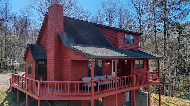 rear view of property with a chimney, a deck, and roof with shingles