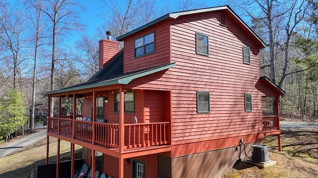 rear view of house with a chimney, a deck, and cooling unit