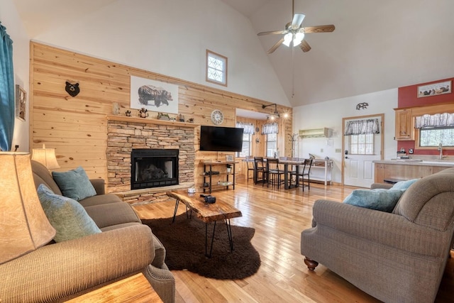 living room with a fireplace, light wood finished floors, ceiling fan, wooden walls, and high vaulted ceiling
