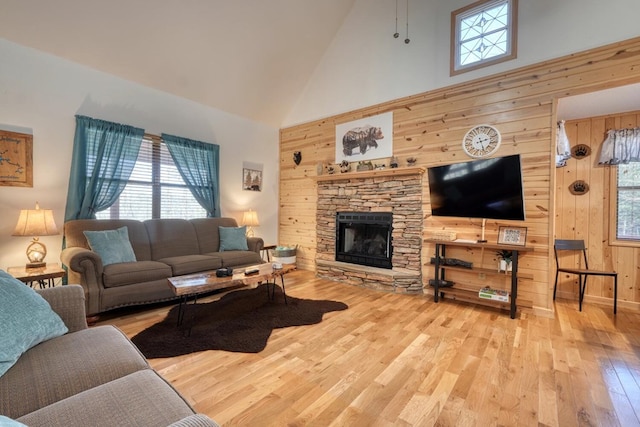 living room with a fireplace, a towering ceiling, light wood-style flooring, and wooden walls