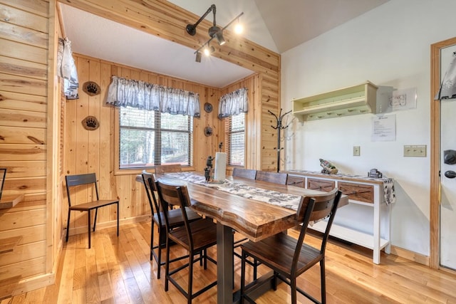 dining room featuring lofted ceiling, wood walls, baseboards, and light wood finished floors
