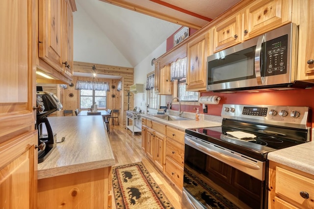 kitchen featuring high vaulted ceiling, stainless steel appliances, a sink, light countertops, and light wood finished floors