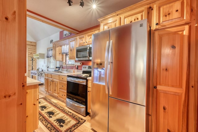 kitchen with light wood finished floors, lofted ceiling, appliances with stainless steel finishes, light countertops, and a sink