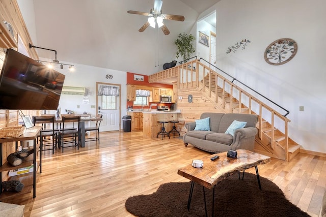 living room with stairway, ceiling fan, light wood-style flooring, and a towering ceiling