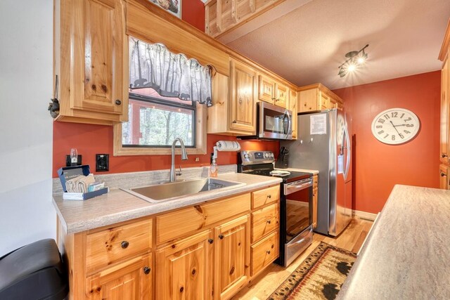 kitchen featuring light wood finished floors, baseboards, appliances with stainless steel finishes, light countertops, and a sink