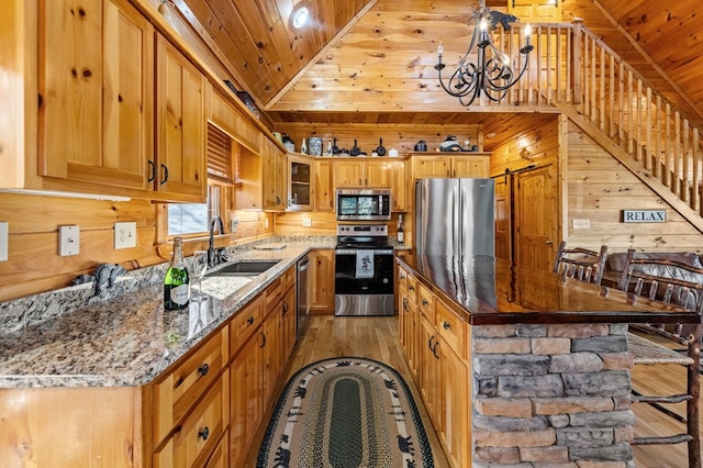 kitchen featuring sink, wood walls, light stone counters, wooden ceiling, and appliances with stainless steel finishes