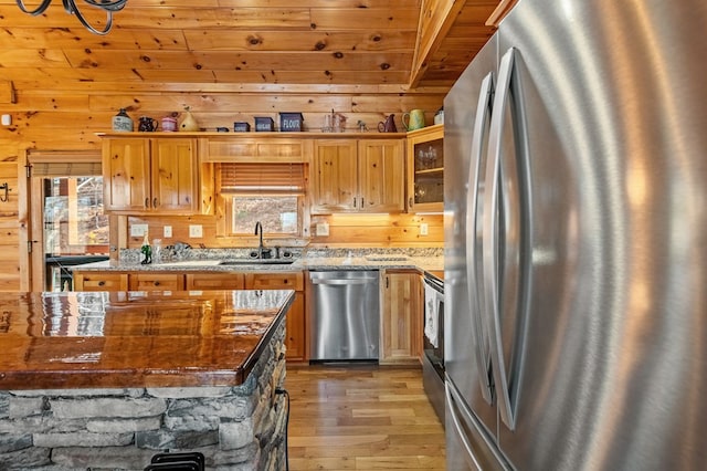 kitchen featuring sink, wood walls, light wood-type flooring, appliances with stainless steel finishes, and light stone countertops