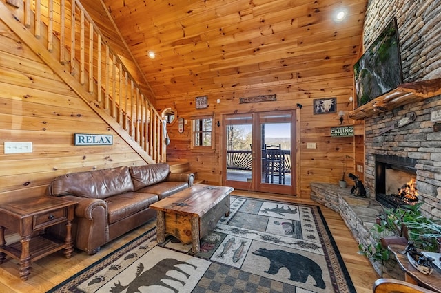 living room with high vaulted ceiling, light hardwood / wood-style floors, a stone fireplace, wooden ceiling, and wood walls