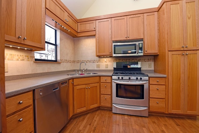 kitchen featuring stainless steel appliances, vaulted ceiling, sink, and light hardwood / wood-style floors