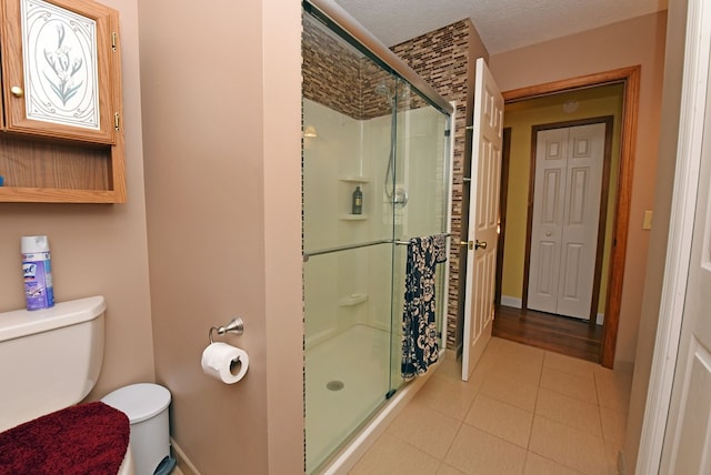 bathroom featuring tile patterned flooring, a textured ceiling, toilet, and walk in shower