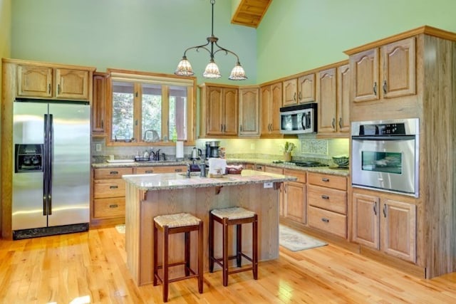 kitchen with light stone counters, a kitchen island, high vaulted ceiling, light hardwood / wood-style floors, and stainless steel appliances