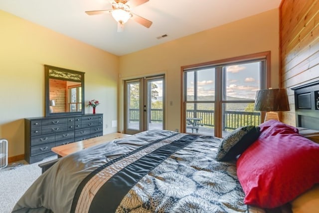 carpeted bedroom featuring multiple windows, wood walls, access to exterior, and ceiling fan