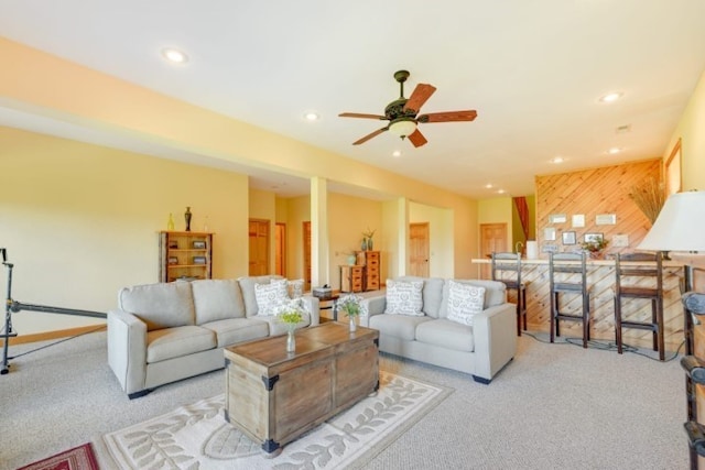 carpeted living room featuring wooden walls and ceiling fan