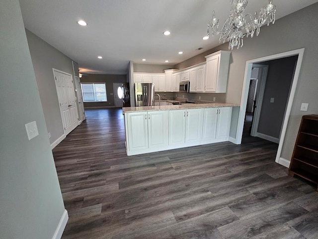 kitchen with kitchen peninsula, appliances with stainless steel finishes, light stone counters, dark wood-type flooring, and white cabinets