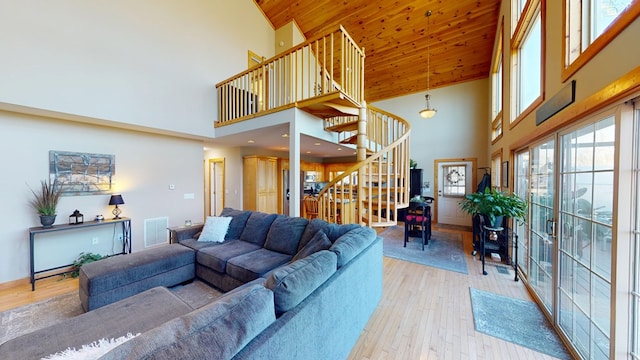 living area featuring visible vents, stairs, light wood-style flooring, and high vaulted ceiling