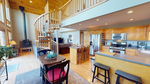 kitchen with a wood stove, appliances with stainless steel finishes, light wood-style flooring, and a towering ceiling