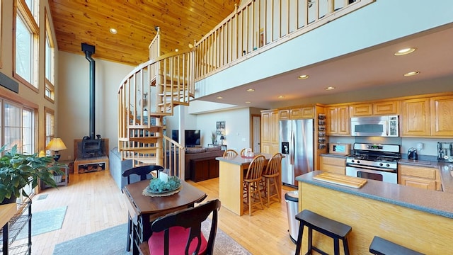 kitchen with a breakfast bar, a wood stove, stainless steel appliances, and a high ceiling