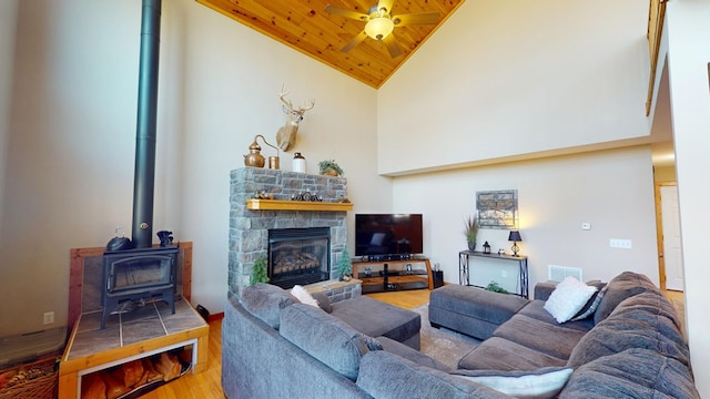 living room with wood finished floors, wood ceiling, a fireplace, a wood stove, and a ceiling fan