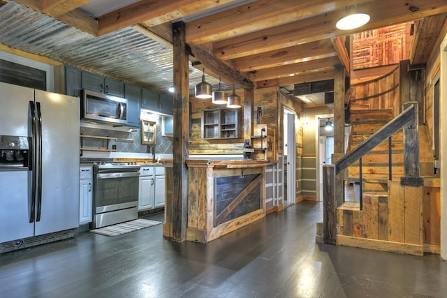 kitchen featuring stainless steel appliances, wood walls, tasteful backsplash, beam ceiling, and decorative light fixtures