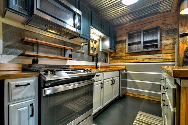 kitchen featuring white cabinets, wood walls, appliances with stainless steel finishes, and tasteful backsplash