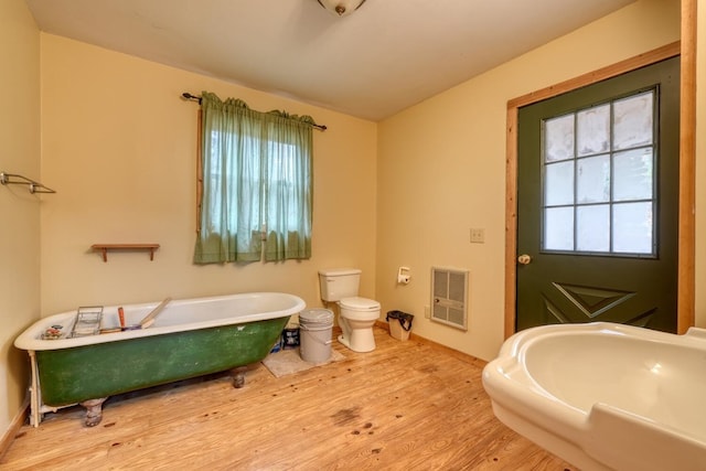 bathroom with a bathtub, heating unit, sink, hardwood / wood-style floors, and toilet