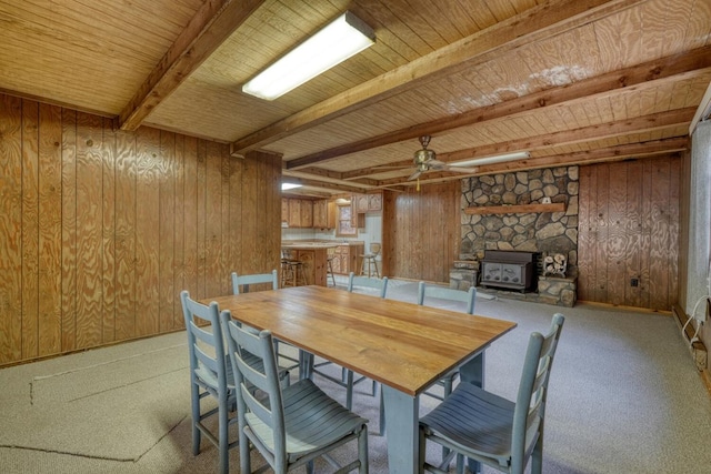 carpeted dining area featuring a wood stove, wooden walls, ceiling fan, and wood ceiling