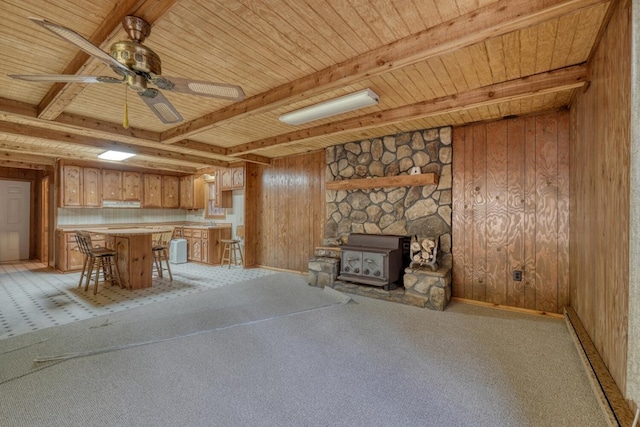 unfurnished living room featuring wood walls, ceiling fan, light carpet, and a wood stove