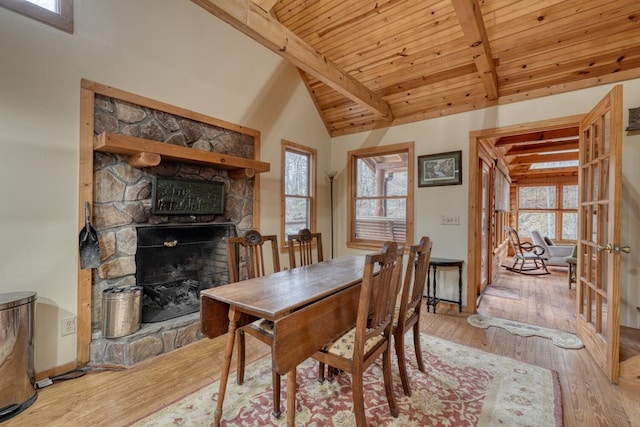 dining area featuring a stone fireplace, wood ceiling, high vaulted ceiling, beam ceiling, and light hardwood / wood-style flooring