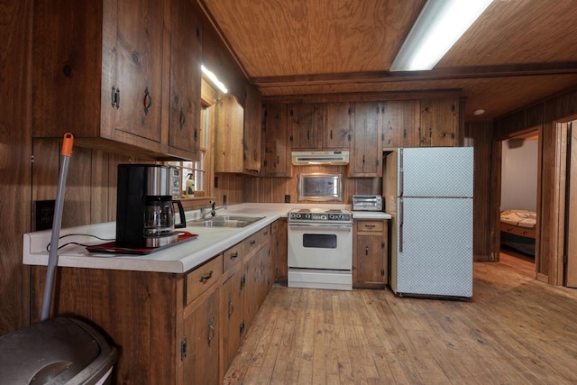 kitchen featuring white appliances, wooden walls, sink, and light wood-type flooring