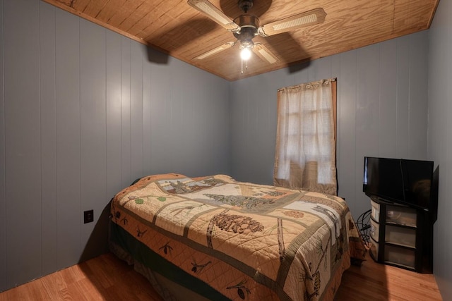 bedroom featuring wooden walls, hardwood / wood-style flooring, ceiling fan, and wooden ceiling