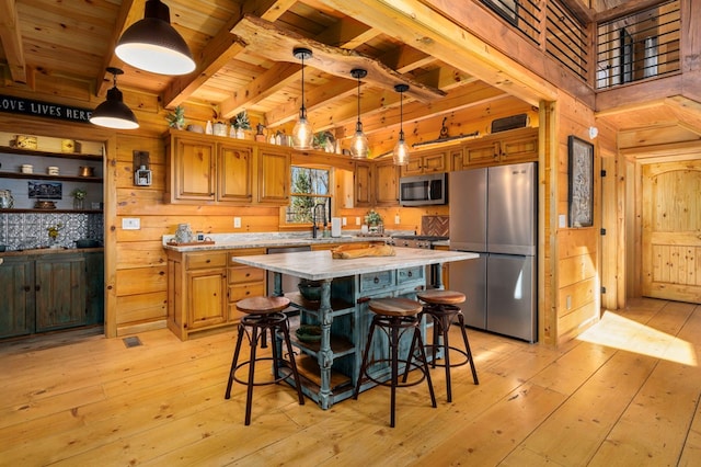 kitchen with appliances with stainless steel finishes, pendant lighting, a kitchen bar, a center island, and light stone counters