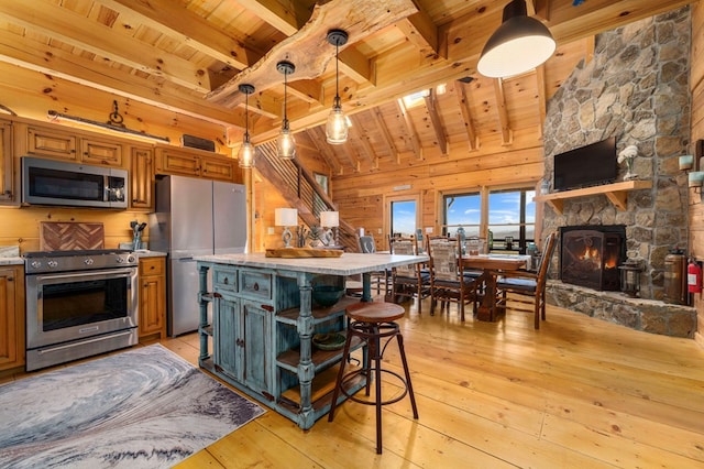 kitchen featuring a stone fireplace, wood ceiling, a kitchen breakfast bar, pendant lighting, and stainless steel appliances