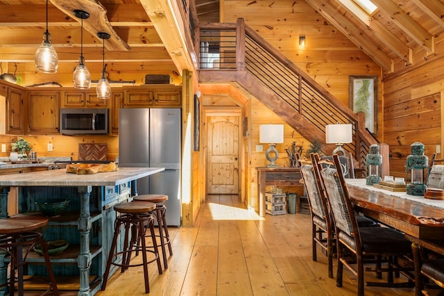 kitchen with a breakfast bar area, wood walls, decorative light fixtures, light wood-type flooring, and appliances with stainless steel finishes