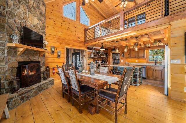 dining room featuring ceiling fan, light hardwood / wood-style flooring, a fireplace, and wood walls