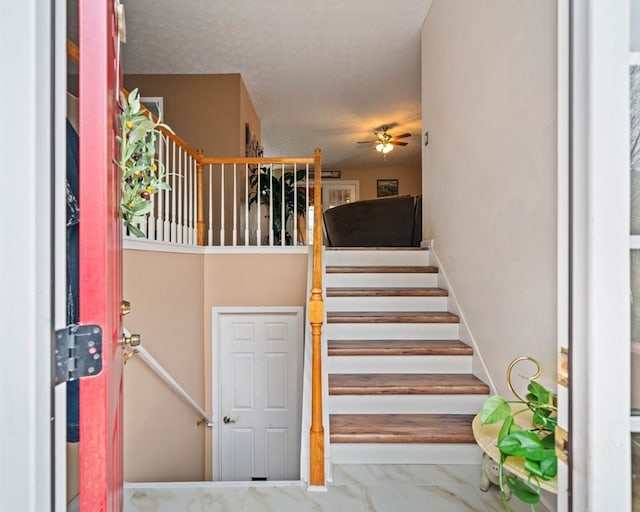 stairs with a textured ceiling and ceiling fan