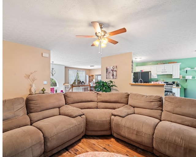 living room with ceiling fan, a textured ceiling, and light wood-type flooring