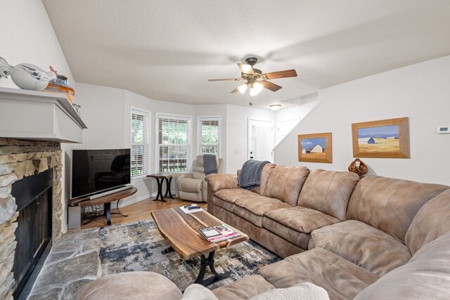 living room with light wood-type flooring, ceiling fan, a fireplace, and a textured ceiling