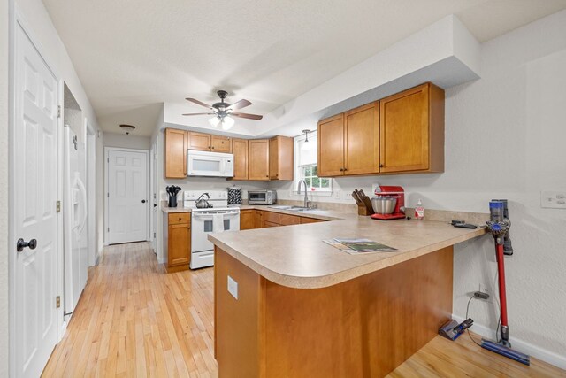 kitchen with light wood-type flooring, sink, kitchen peninsula, white appliances, and ceiling fan