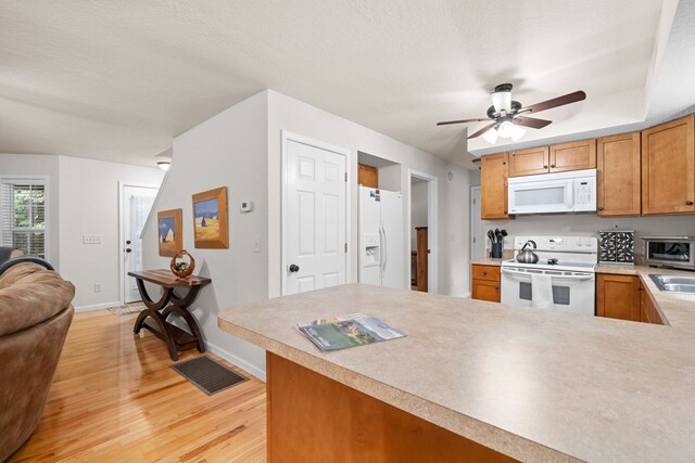 kitchen with light hardwood / wood-style floors, a textured ceiling, kitchen peninsula, white appliances, and ceiling fan