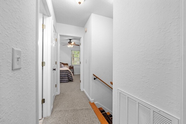 corridor featuring a textured ceiling and light colored carpet