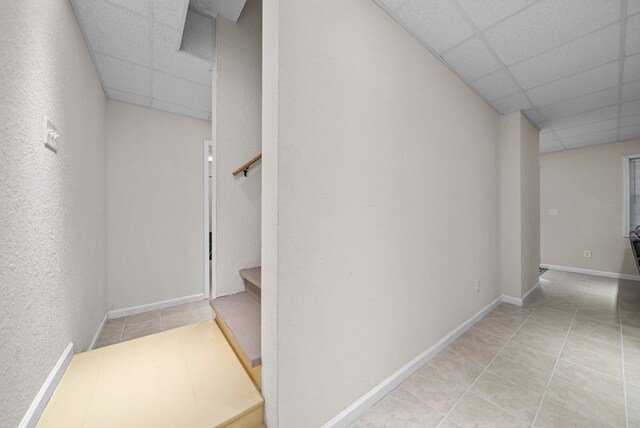 corridor featuring light tile patterned floors and a paneled ceiling