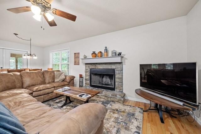 living room with ceiling fan with notable chandelier, a fireplace, and hardwood / wood-style floors