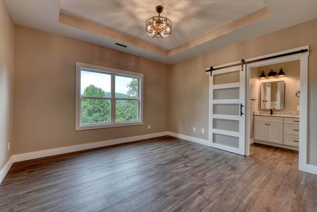 unfurnished bedroom featuring connected bathroom, a raised ceiling, and a barn door