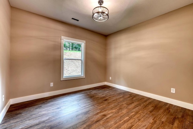 empty room featuring wood-type flooring and an inviting chandelier