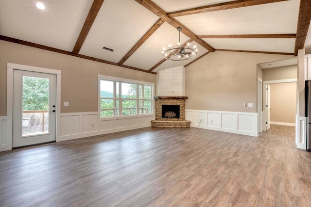 unfurnished living room with a notable chandelier, a stone fireplace, lofted ceiling with beams, and hardwood / wood-style flooring