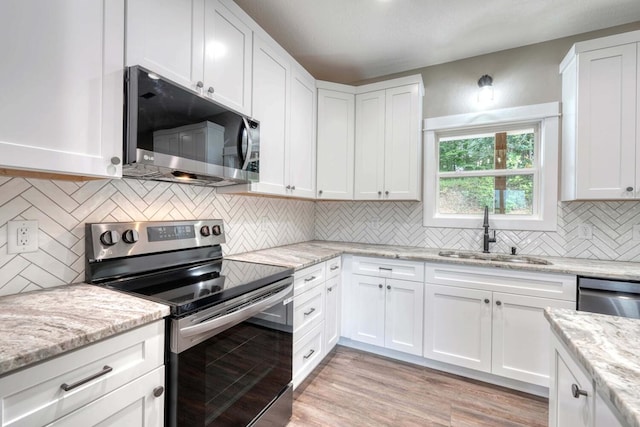 kitchen featuring appliances with stainless steel finishes, sink, white cabinets, light stone countertops, and light hardwood / wood-style flooring