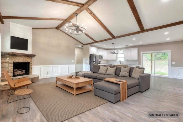 living room featuring sink, a notable chandelier, a fireplace, lofted ceiling with beams, and light wood-type flooring