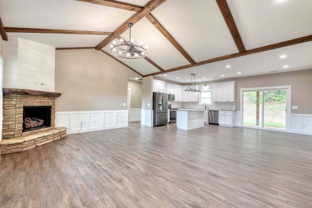 unfurnished living room featuring sink, hardwood / wood-style flooring, vaulted ceiling with beams, a notable chandelier, and a stone fireplace